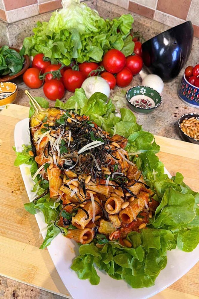 Rigatoni alla Siciliana served in a roasted eggplant bowl with tomato sauce, fried eggplant, toasted pine nuts, Parmesan cheese, basil, and fresh lettuce