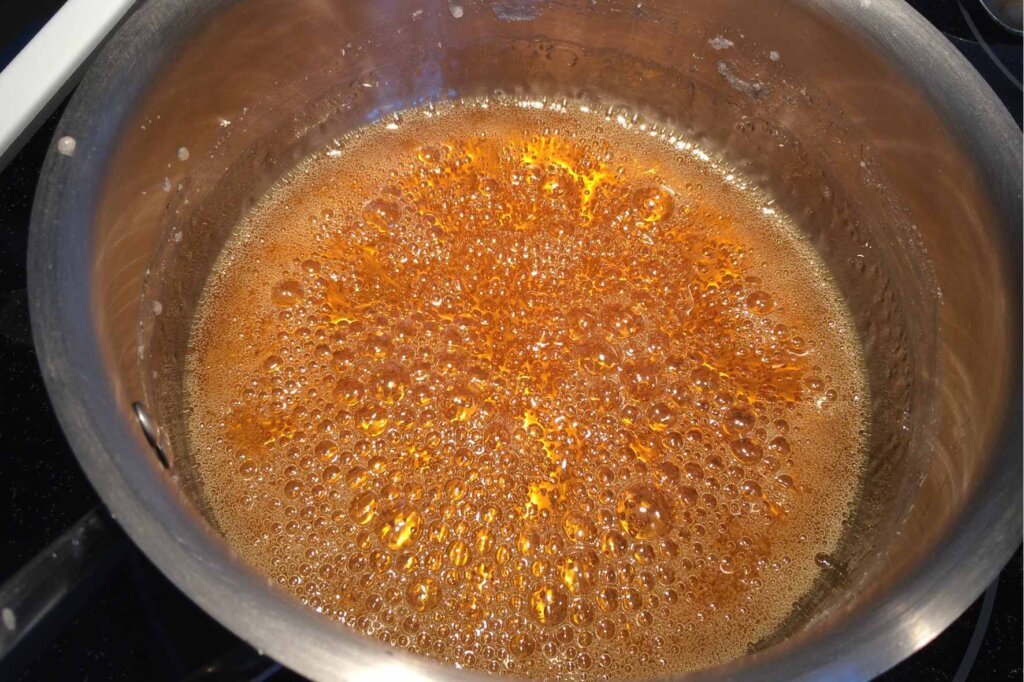 Homemade caramel sauce cooking in a saucepan as the sugar reaches a rich amber color during caramelization