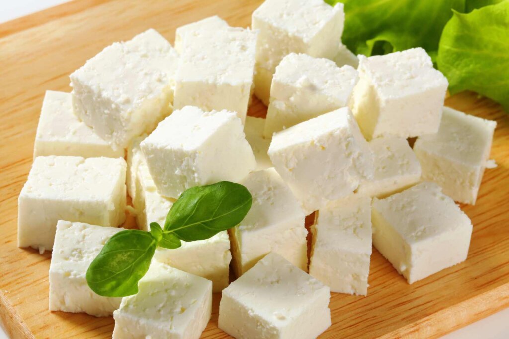 Cubed feta cheese on a wooden board for a crispy quinoa kale salad.