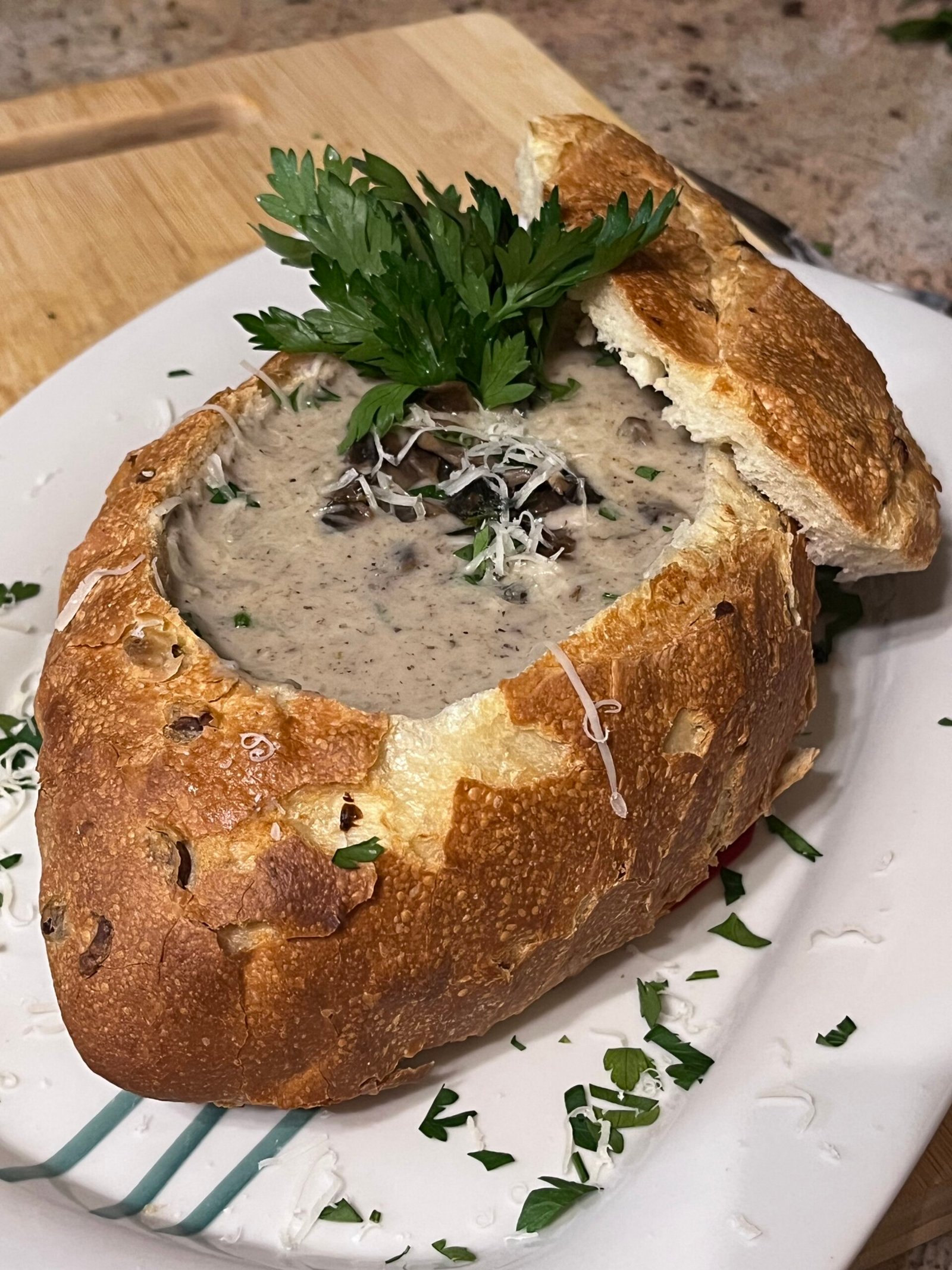 a creamy mushroom soup served in a sourdough bowl decorated with parsley and parmesan