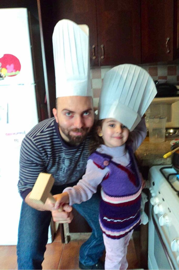 Chef François and his four-year-old daughter Nour wearing chef hats while cooking together at home.