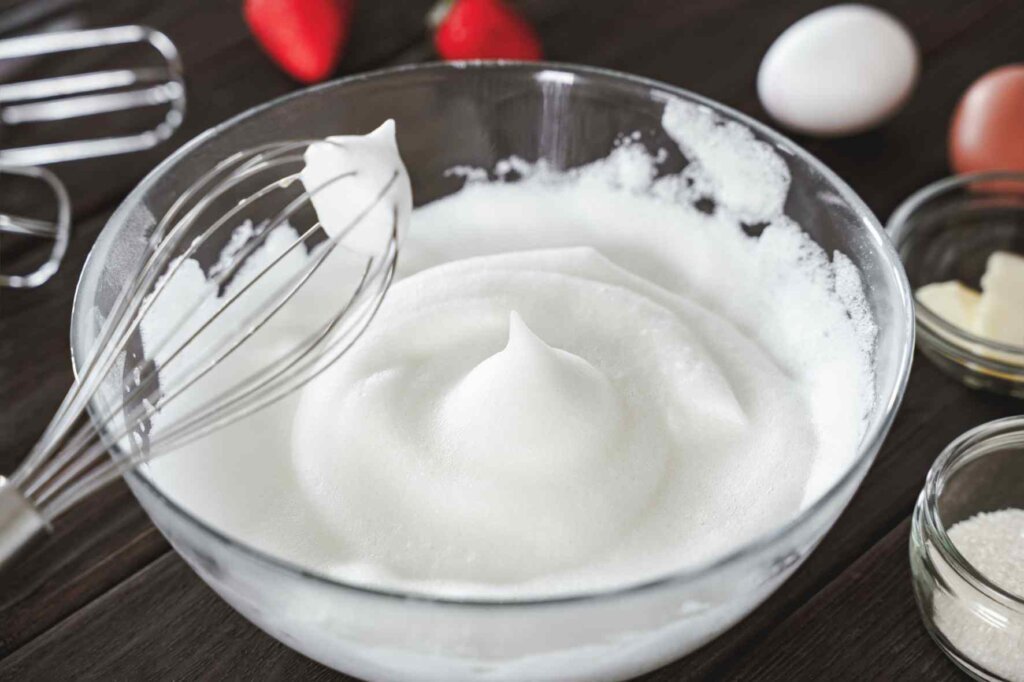 Italian meringue whipped to stiff peaks in a glass bowl before adding 121°C sugar syrup for authentic tiramisu.