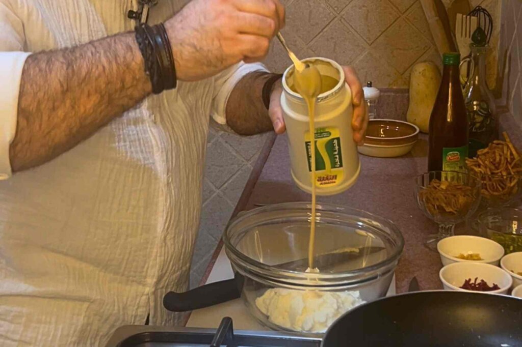 Chef François pouring tahini into yogurt to prepare the creamy sauce for authentic Lebanese chickpea fatteh.