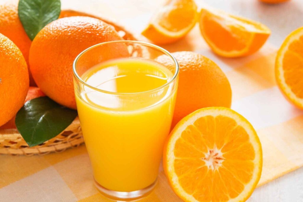 Glass of fresh orange juice surrounded by whole and sliced oranges for pumpkin soup recipe