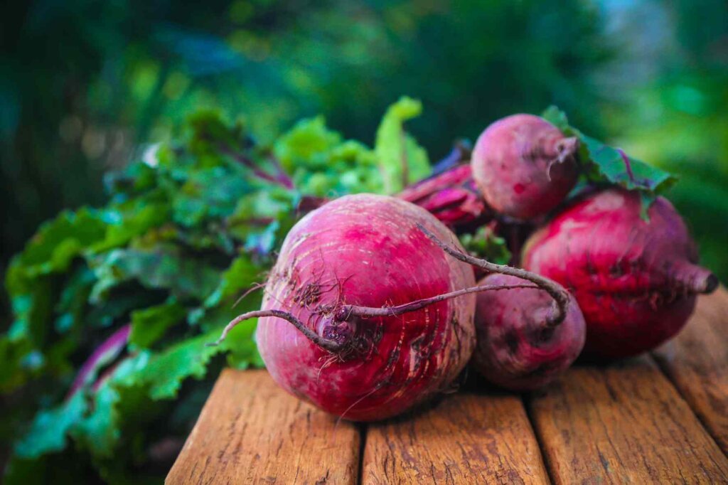 Fresh whole beetroots with green leaves arranged on a rustic wooden table.