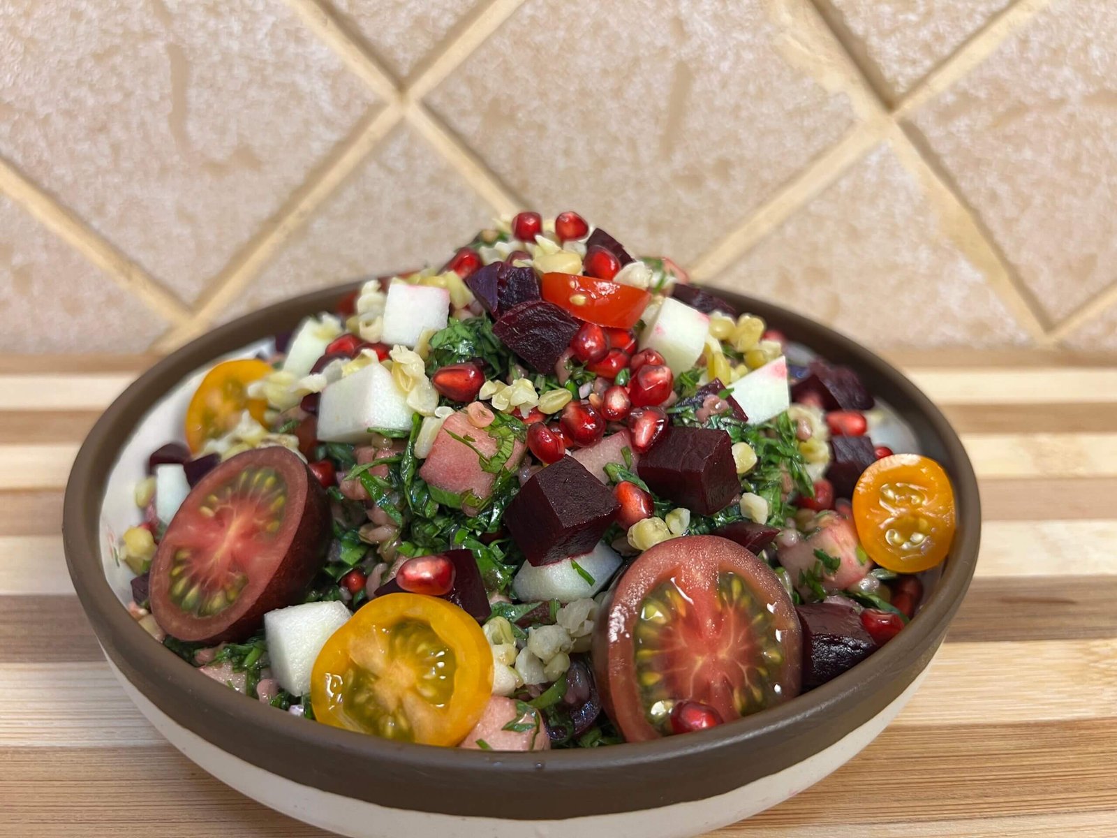 Close-up of a colorful freekeh tabbouleh salad with parsley, pomegranate seeds, beetroot, cherry tomatoes, and diced green apple served in a bowl.