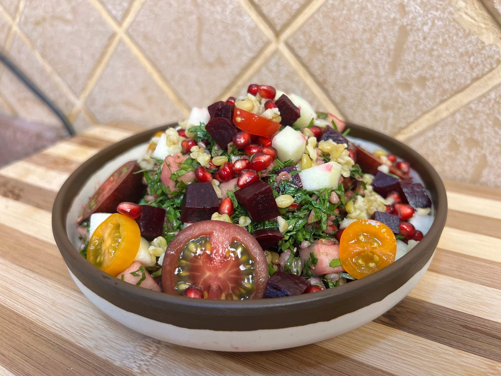 Close-up of a colorful freekeh tabbouleh salad with parsley, pomegranate seeds, beetroot, cherry tomatoes, and diced green apple served in a bowl.