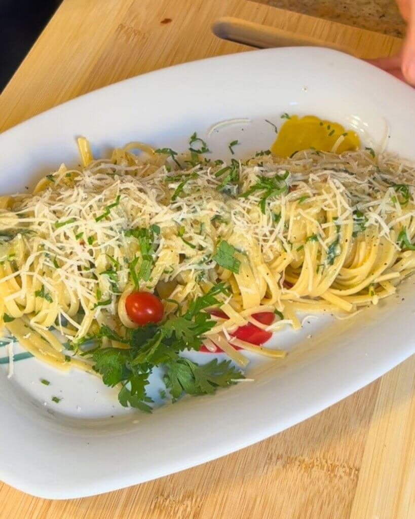 Aglio e olio linguine pasta plated with grated Parmesan cheese, fresh parsley, and cherry tomatoes on a white dish
