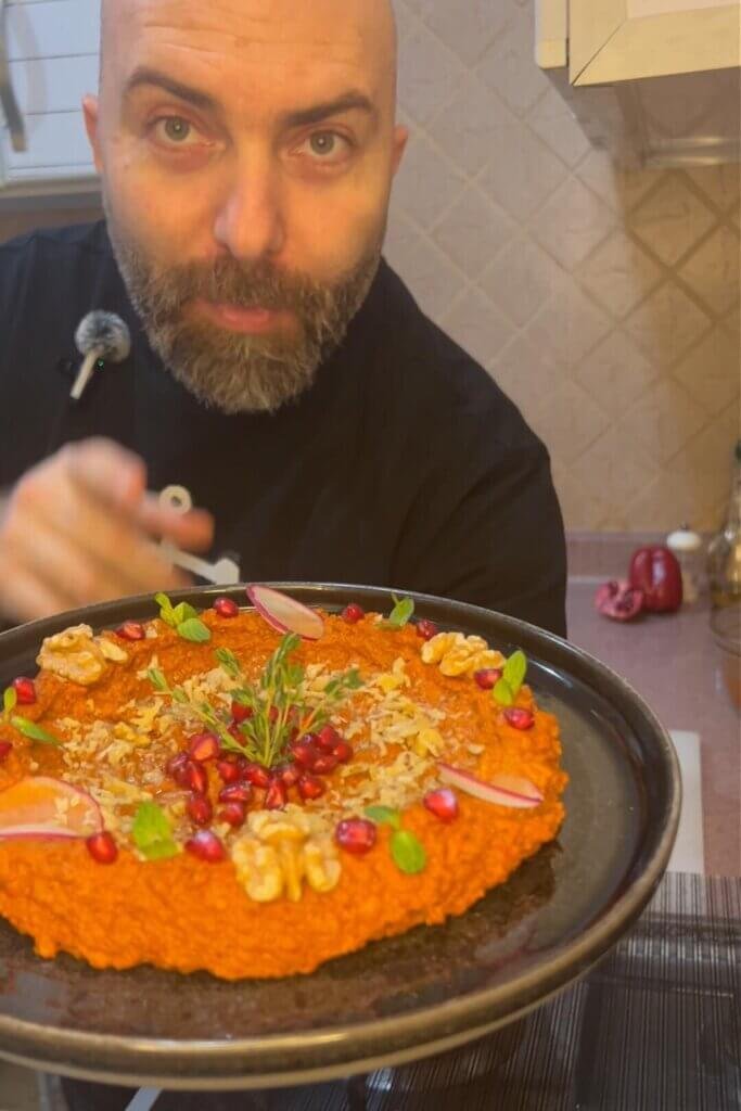 Chef holding a plate of easy Muhammara dip garnished with walnuts, pomegranate seeds, and herbs