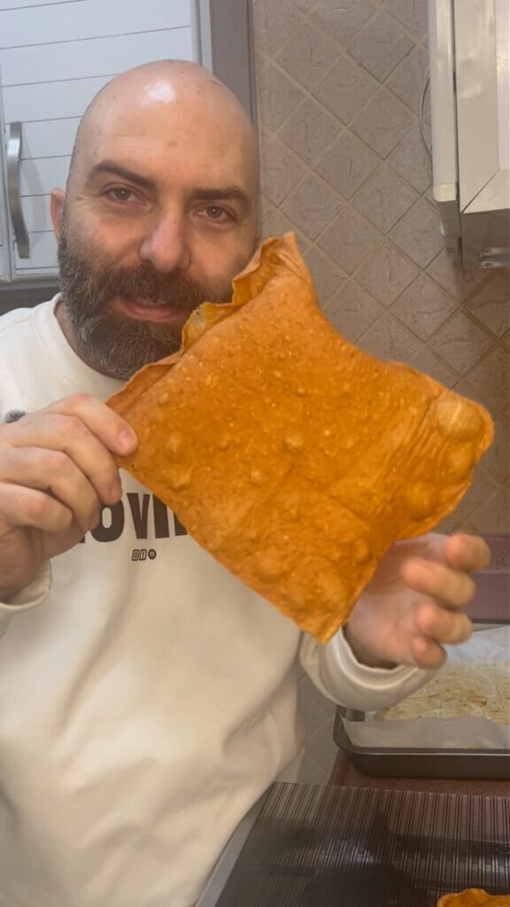 Chef François holding a crispy high protein chicken cracker, showing its thin texture and golden color in a kitchen setting