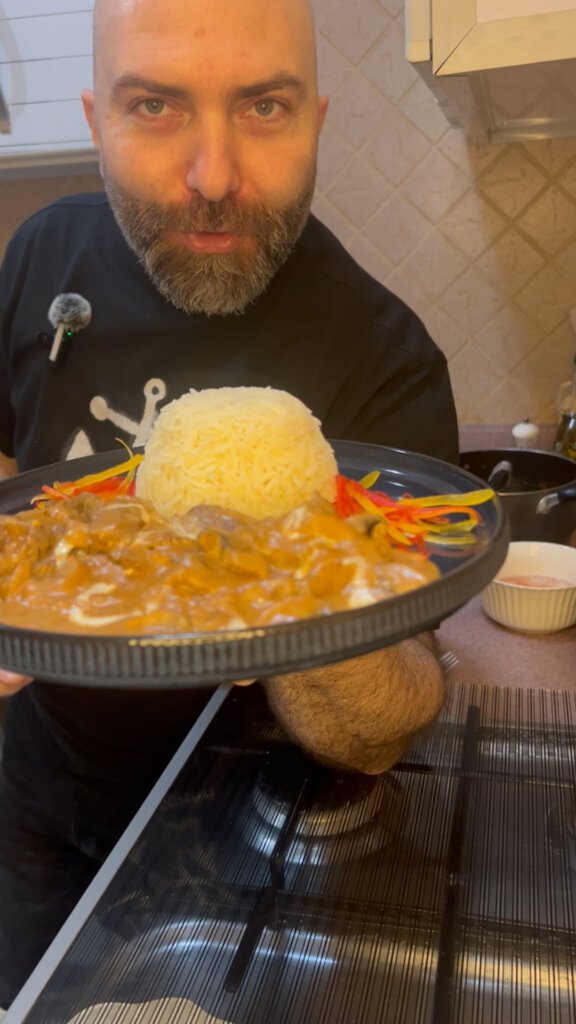 Chef holding creamy beef stroganoff with rice and vegetables in a home kitchen