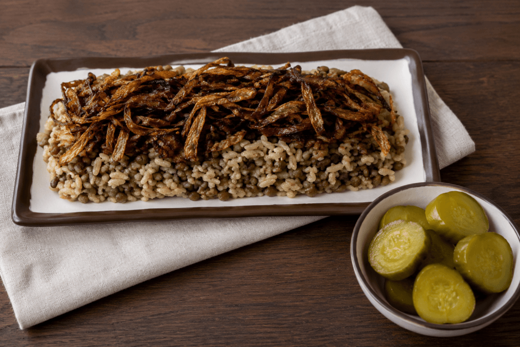 Traditional Lebanese mdardara made with rice and brown lentils, topped with crispy fried onions and served with cucumber pickles on the side.