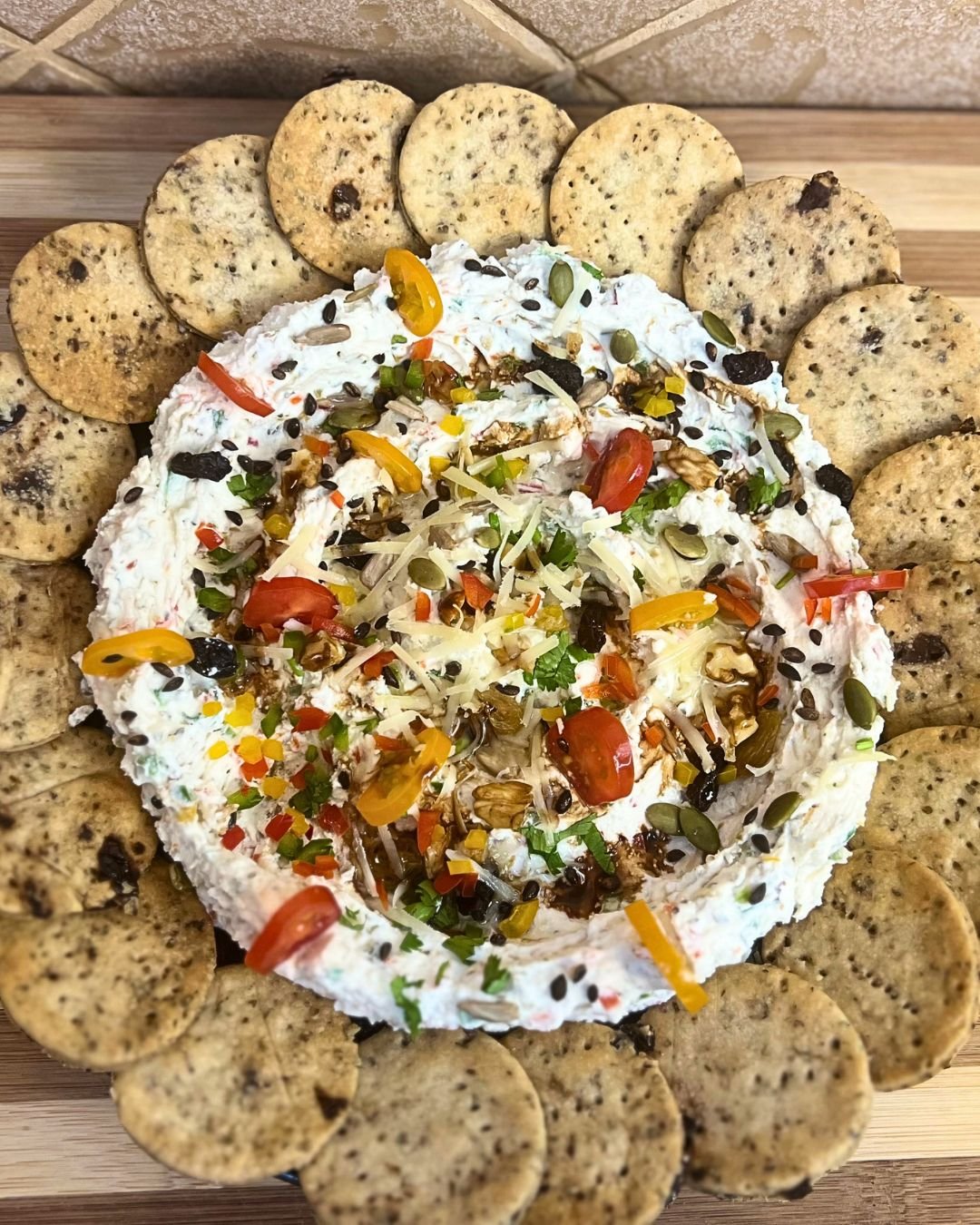 Creamy feta dip topped with vegetables, seeds, walnuts, and balsamic glaze, served with crackers