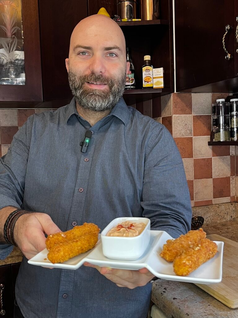 chef holding a plate of crispy mozzarella sticks with cocktail sauce in the middle