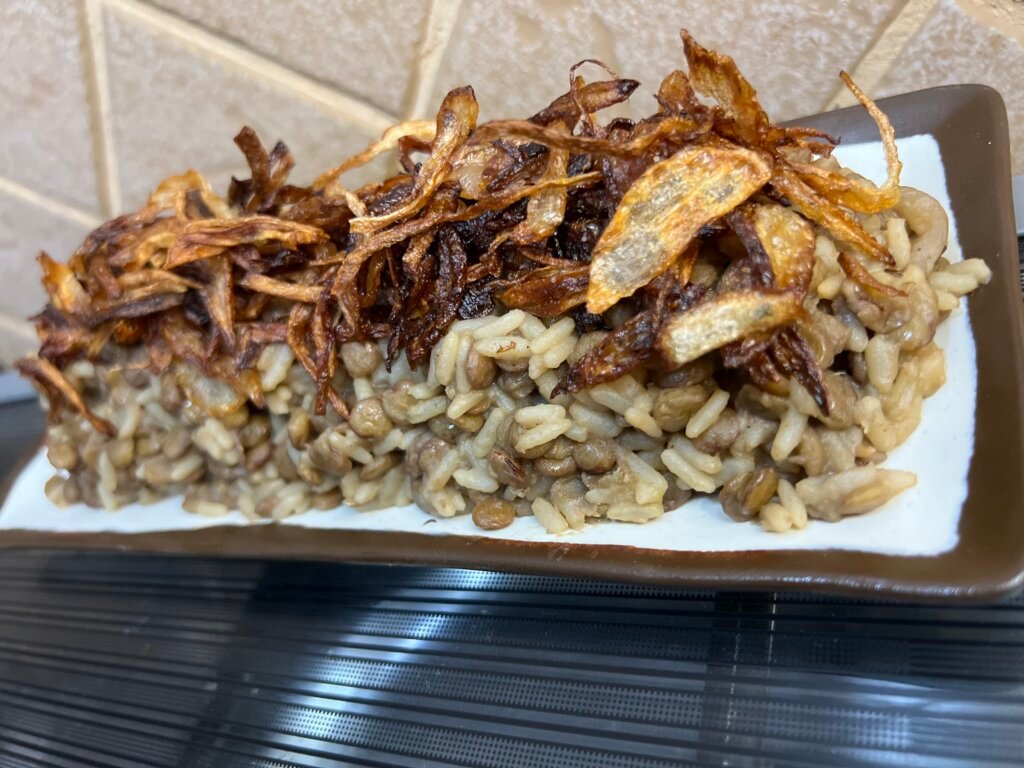 Lebanese mdardara made with lentils and rice, topped with crispy fried onions, served on a rectangular plate