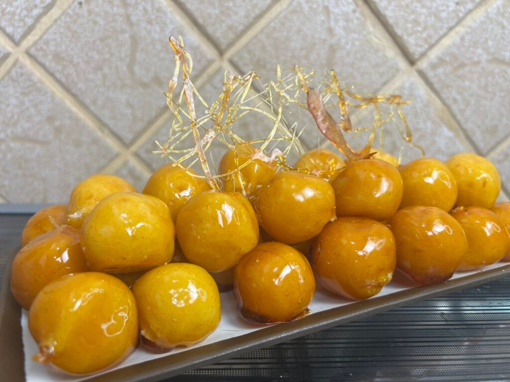 Brazilian bala baiana coconut balls coated in shiny caramel with decorative sugar threads on a white plate