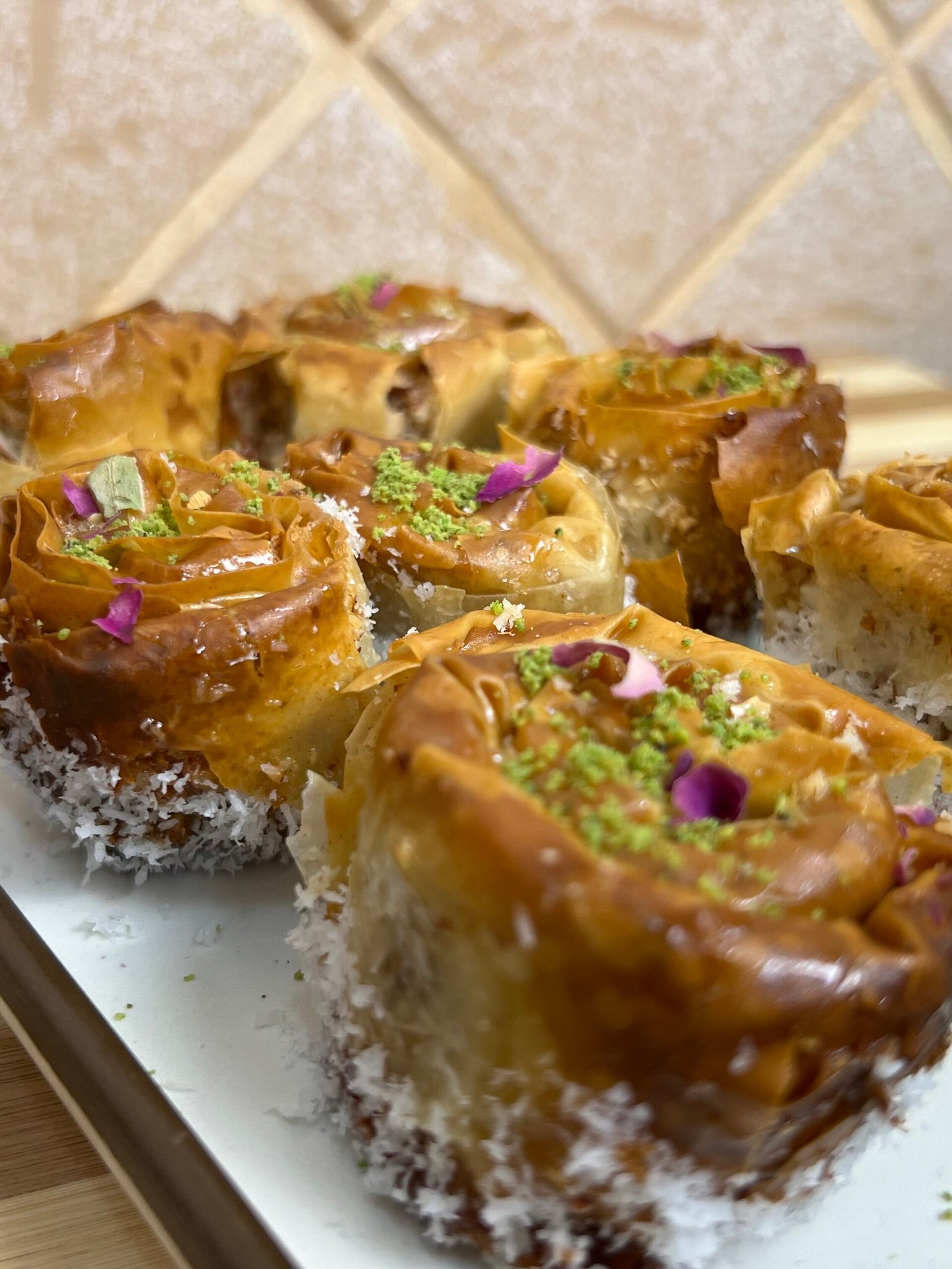 Close-up angled view of crispy baklava roses filled with almonds and coconut, topped with pistachios and rose petals on a plate
