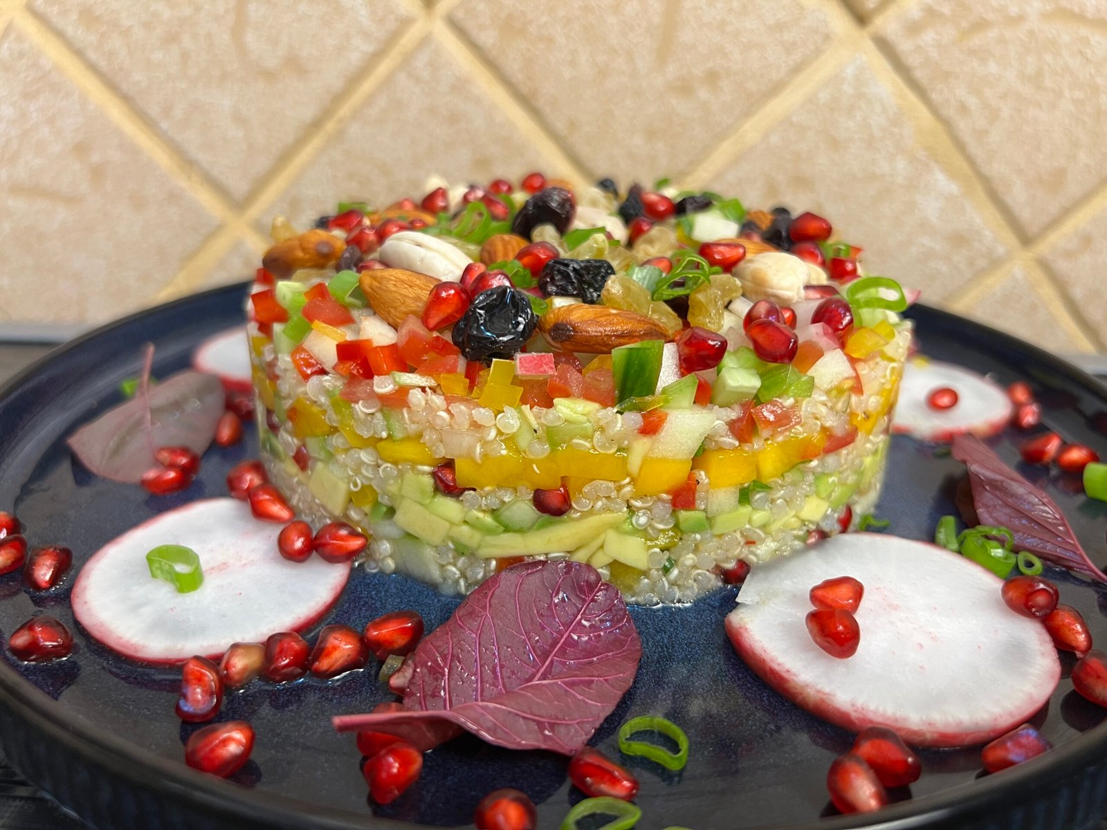 Layered quinoa salad with avocado, mango, cucumber, apple, pomegranate seeds, nuts, and raisins, beautifully plated with radish slices