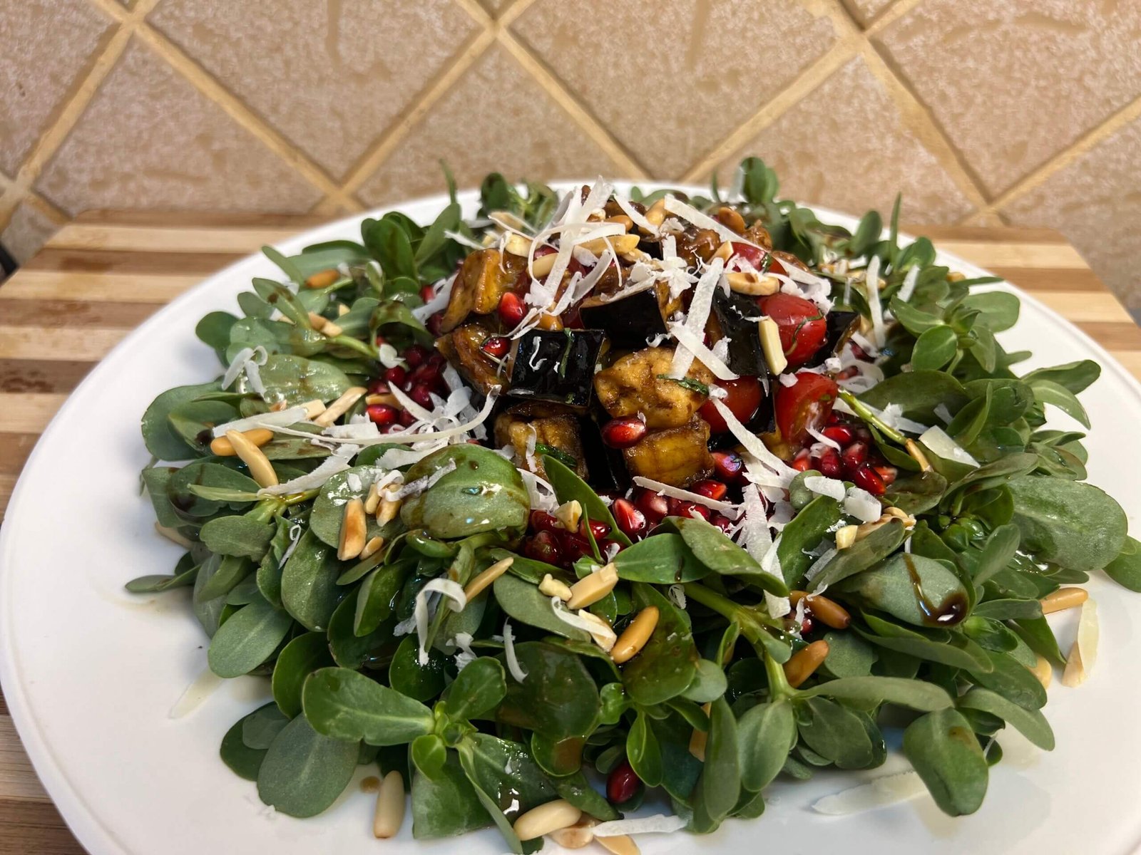 Eggplant and purslane salad arranged in a wreath shape with crispy fried eggplant, cherry tomatoes, pomegranate seeds, and nuts