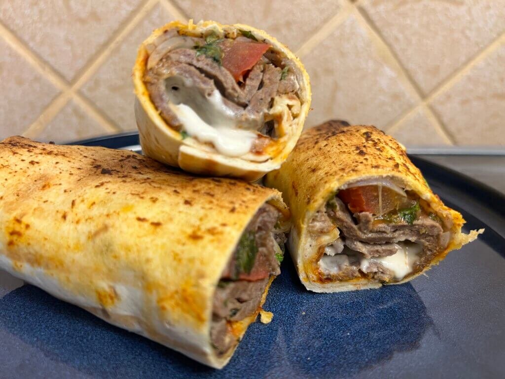 Close-up of a homemade doner kebab wrap showing juicy beef, sauce, and fresh vegetables inside soft bread