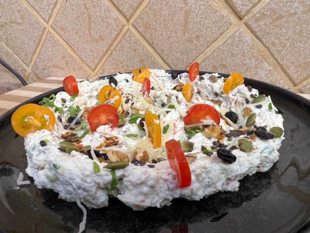 Creamy feta dip spread on a plate topped with cherry tomatoes, seeds, walnuts, herbs, and balsamic glaze