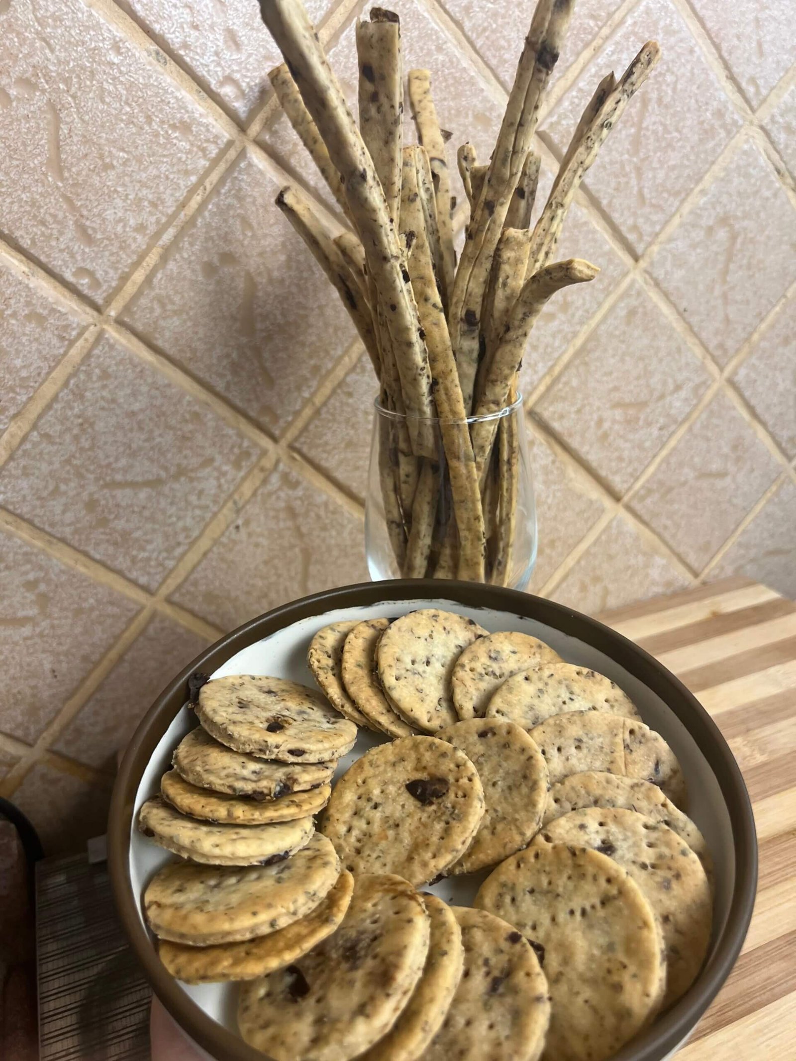 Plate of crispy thyme and olives breadsticks with round crackers arranged on a dish and served in a glass jar