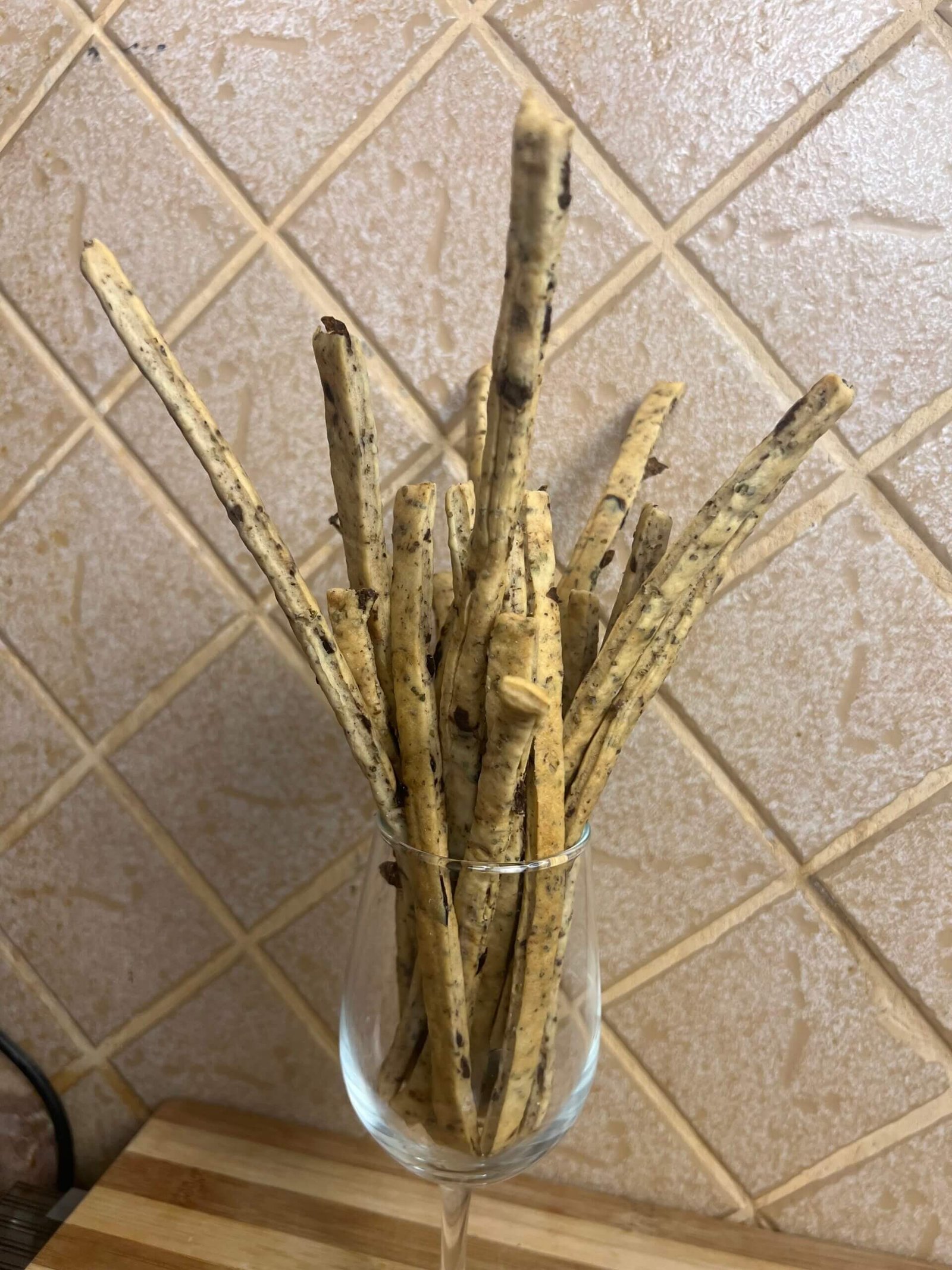 Homemade thyme and olives breadsticks arranged vertically in a glass, showing crispy texture and olive pieces