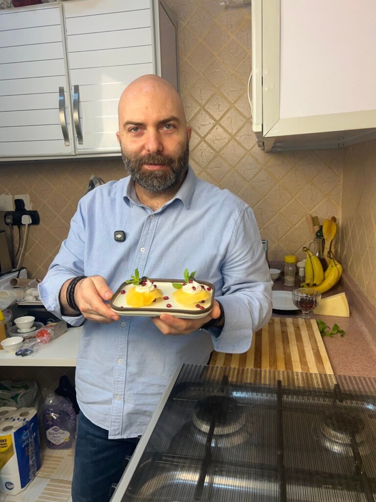 Chef François holding a plate of parmesan eggs topped with labneh, pomegranate, and mint in a home kitchen