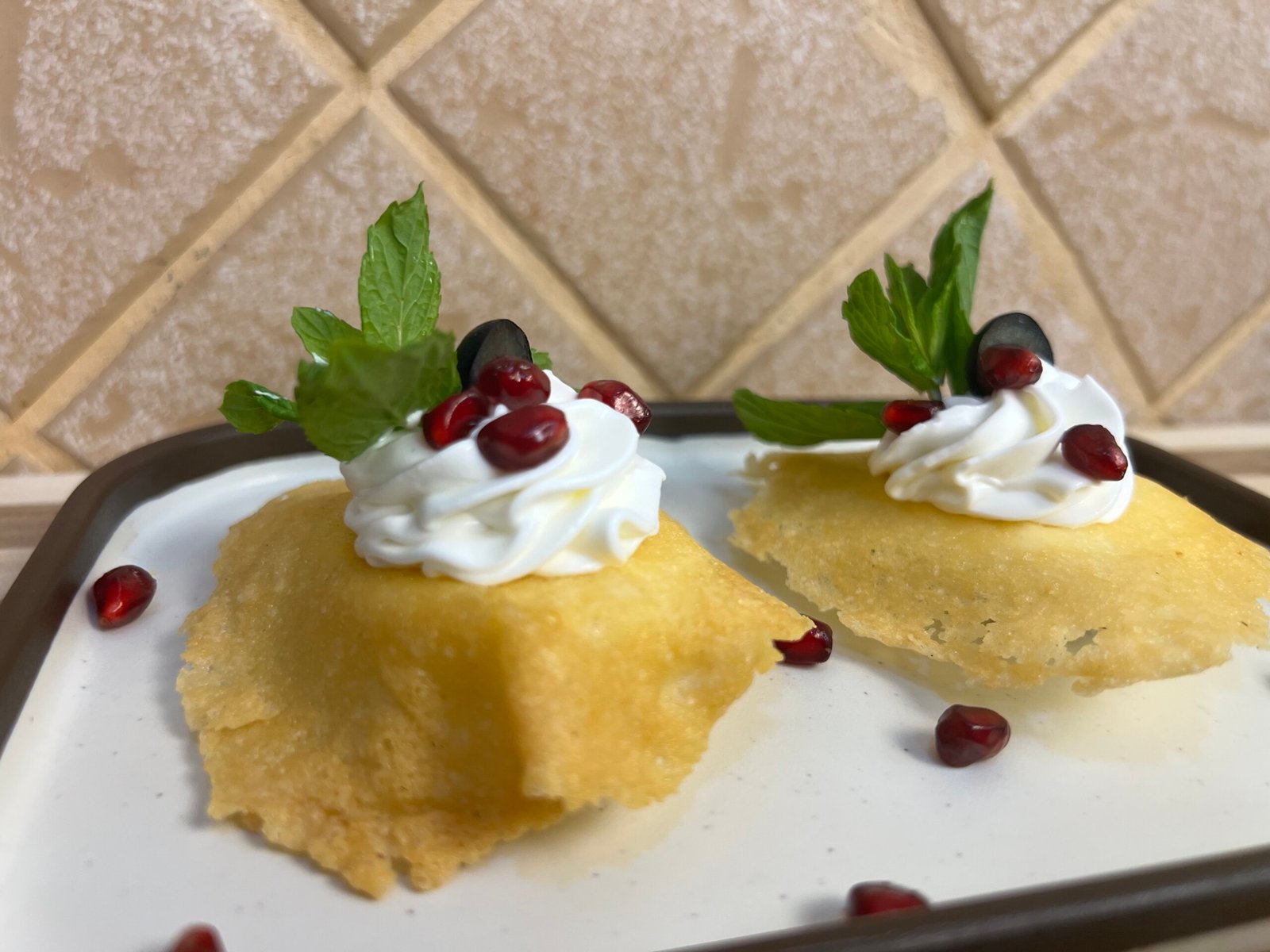 Crispy golden cheese cups topped with whipped cream, pomegranate seeds, mint leaves, and blueberries on a serving plate