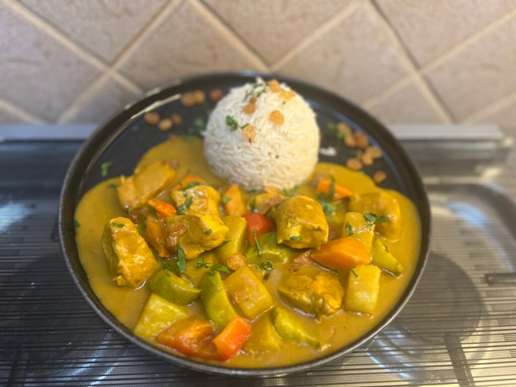 Plate of homemade chicken curry with vegetables served alongside fluffy jasmine rice