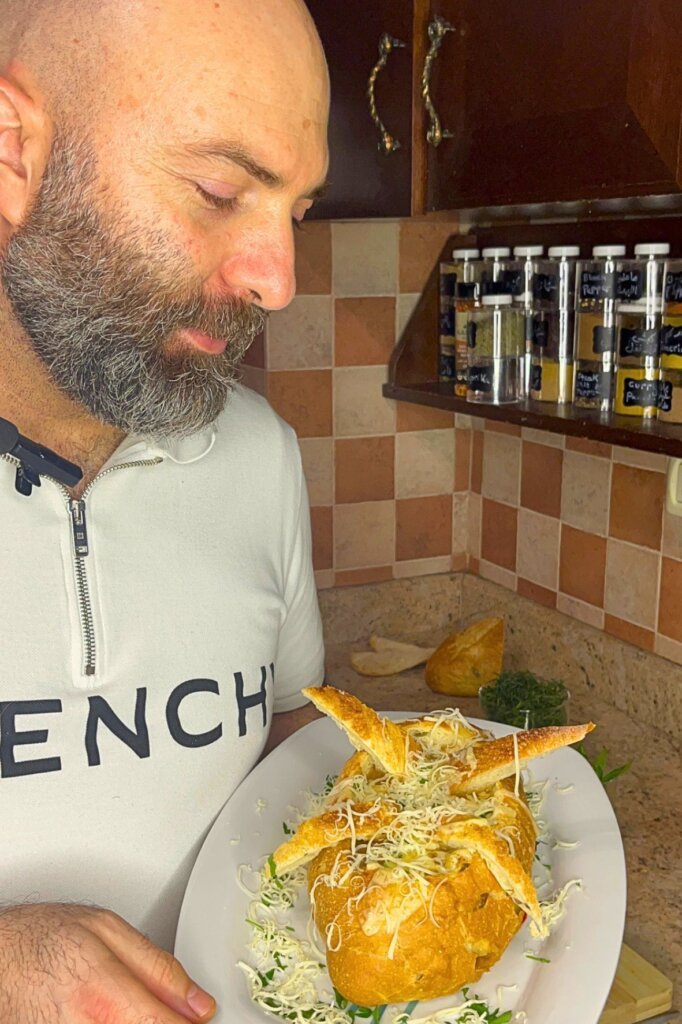 Chef holding a plate with French onion soup in a bread bowl topped with grated cheese