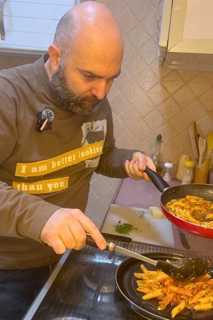 Chef serving penne all'arrabbiata pasta onto a plate from a pan in a home kitchen