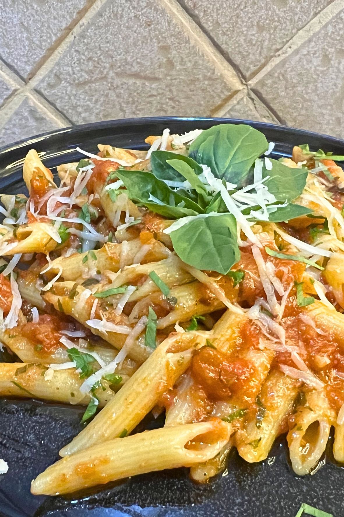 Penne pasta with spicy tomato arrabbiata sauce topped with grated parmesan cheese and fresh basil leaves