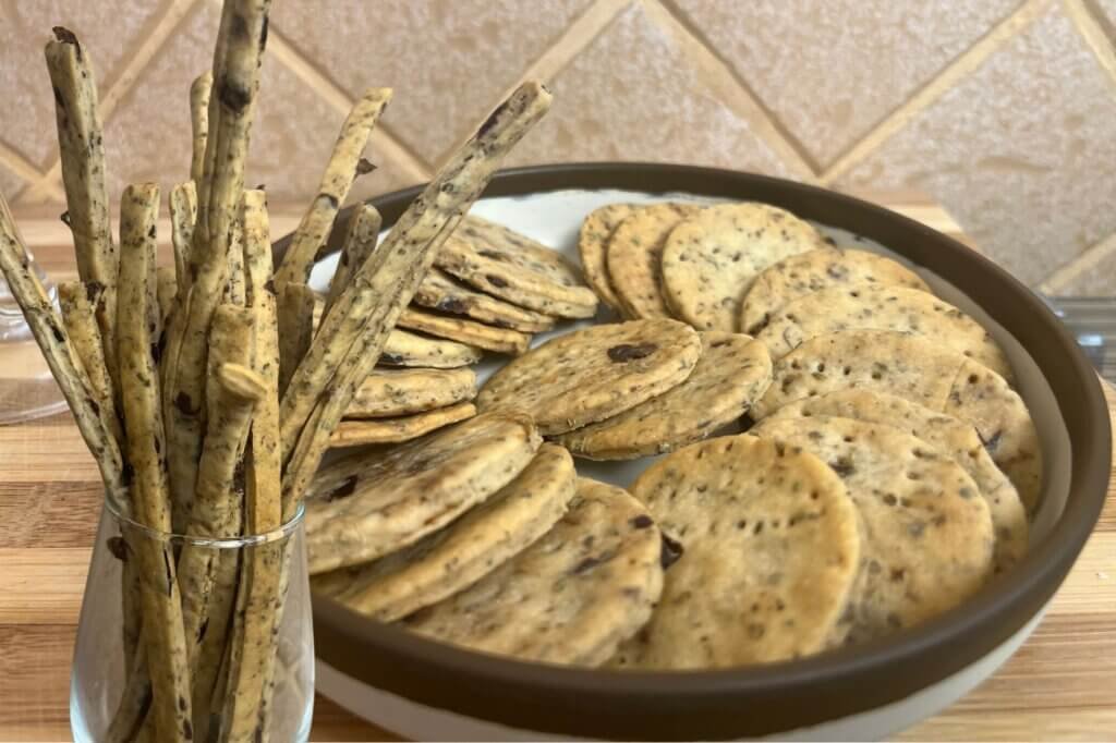 Thyme and olives breadsticks in a glass served with crispy round crackers on a plate