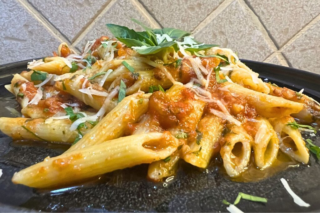 Close-up of penne arrabbiata pasta with tomato sauce, grated parmesan cheese, and fresh basil leaves