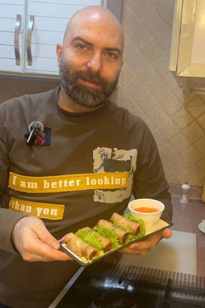 Chef holding a plate of crispy spring rolls served with lettuce and sweet chili dipping sauce