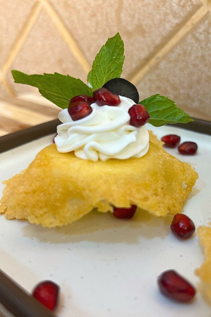 Close-up of Parmesan eggs made of a boiled egg topped with crispy parmesan tuile, labneh cream swirl, pomegranate seeds, and fresh mint leaves