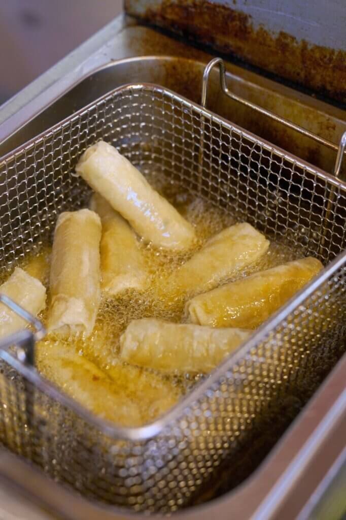 Fresh spring rolls frying in hot oil inside a deep fryer until crispy and golden