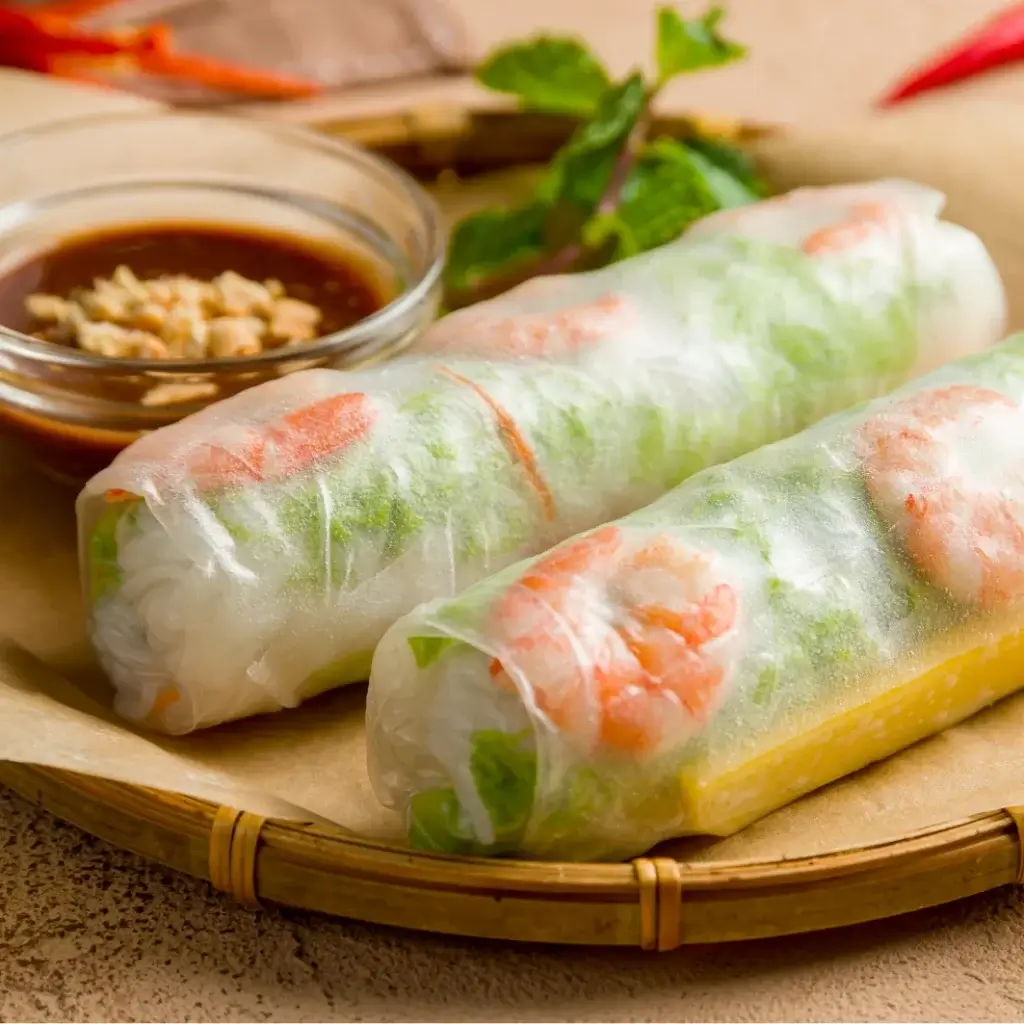 Fresh Vietnamese spring rolls wrapped in rice paper with shrimp and vegetables beside dipping sauce
