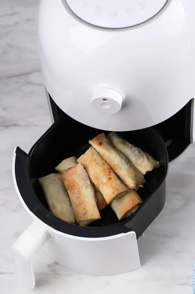 Crunchy spring rolls cooking inside a white air fryer basket until golden brown