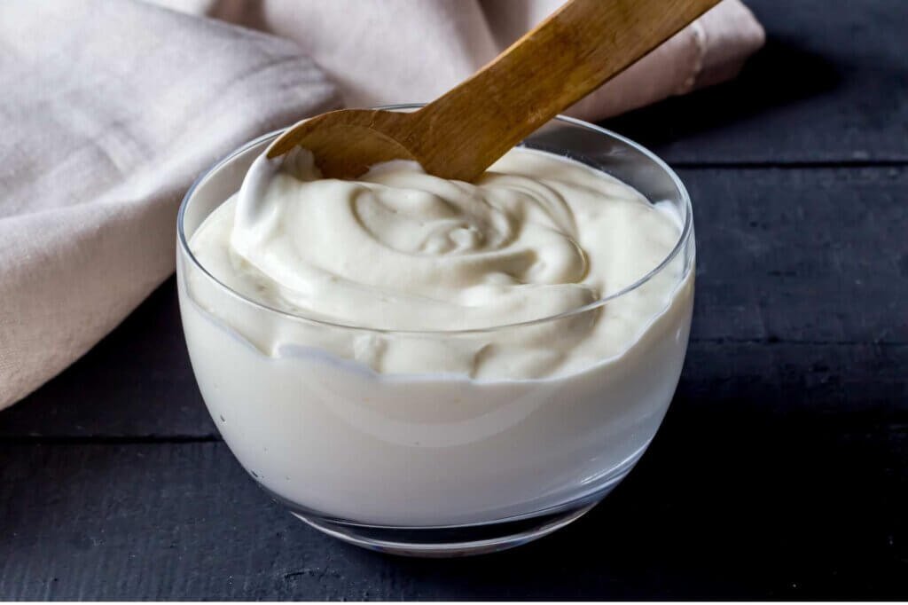 A glass bowl filled with thick, creamy homemade yogurt with a wooden spoon resting on top.