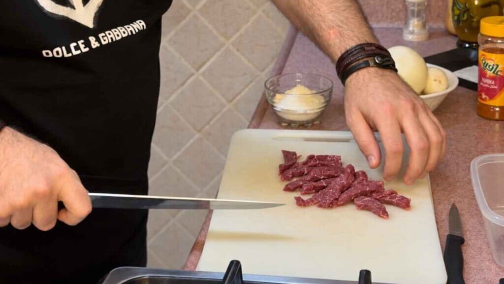 Chef François preparing thin beef tenderloin strips on a white cutting board for beef stroganoff.