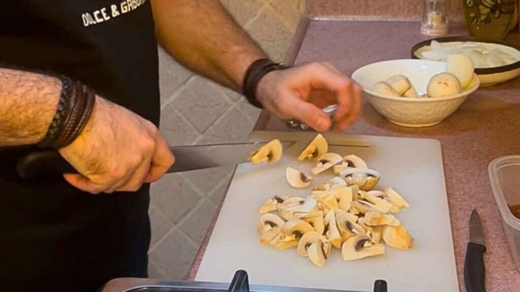 Chef François cutting white button mushrooms into thick pieces on a cutting board for beef stroganoff.