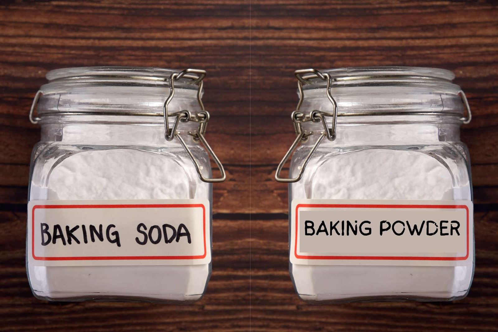 Two glass jars filled with white powder labeled “Baking Soda” and “Baking Powder” side by side on a wooden background, illustrating the difference between common baking leavening agents.