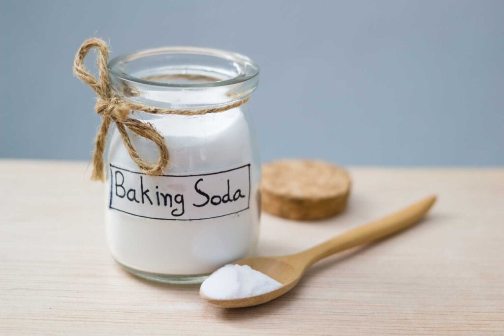 Baking soda vs baking powder comparison showing a glass jar of baking soda and a wooden spoon filled with baking soda powder used in baking recipes.
