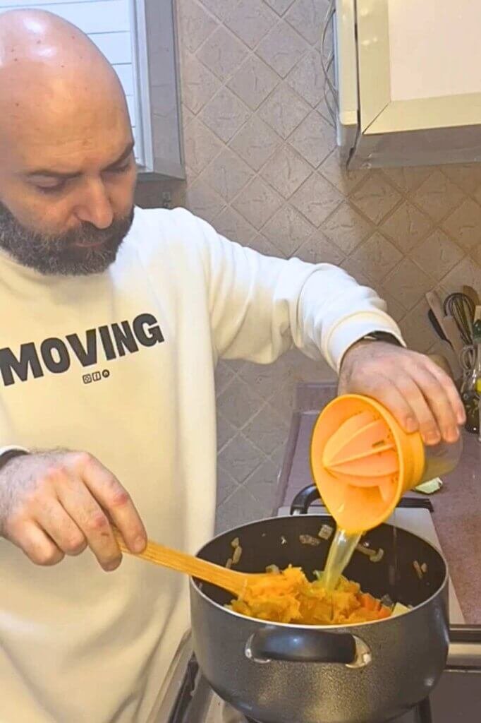 Chef François pouring fresh broth into a pot of pumpkin and vegetables while cooking homemade pumpkin soup in a cozy kitchen.