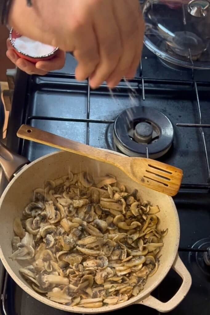 Chef François sprinkling seasoning over sautéed mushrooms cooking in a pan on a stovetop for a flavorful homemade soup recipe.