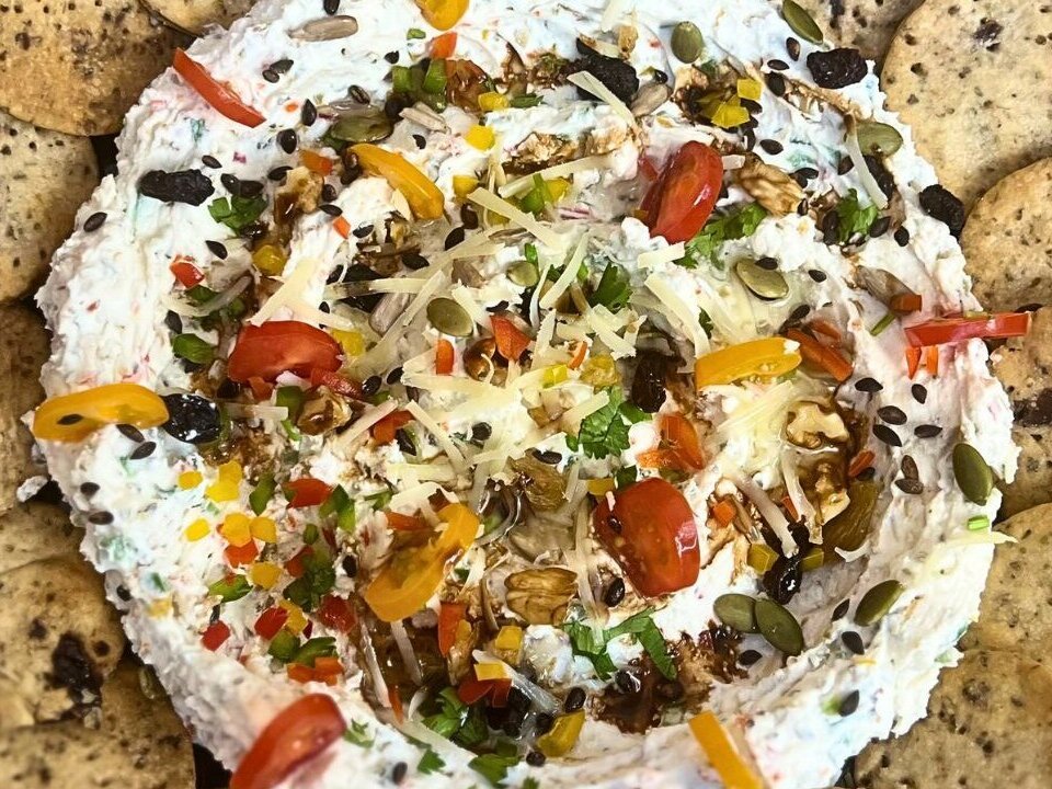 Creamy feta dip topped with vegetables, seeds, walnuts, and balsamic glaze, served with crackers