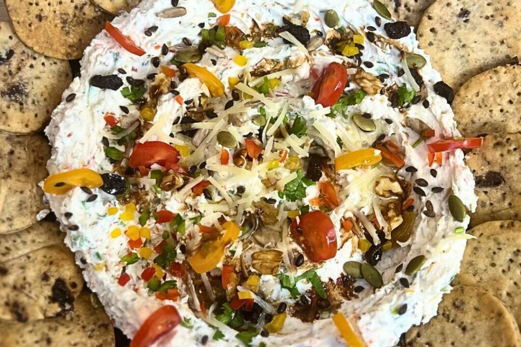 Creamy feta dip topped with vegetables, seeds, walnuts, and balsamic glaze, served with crackers