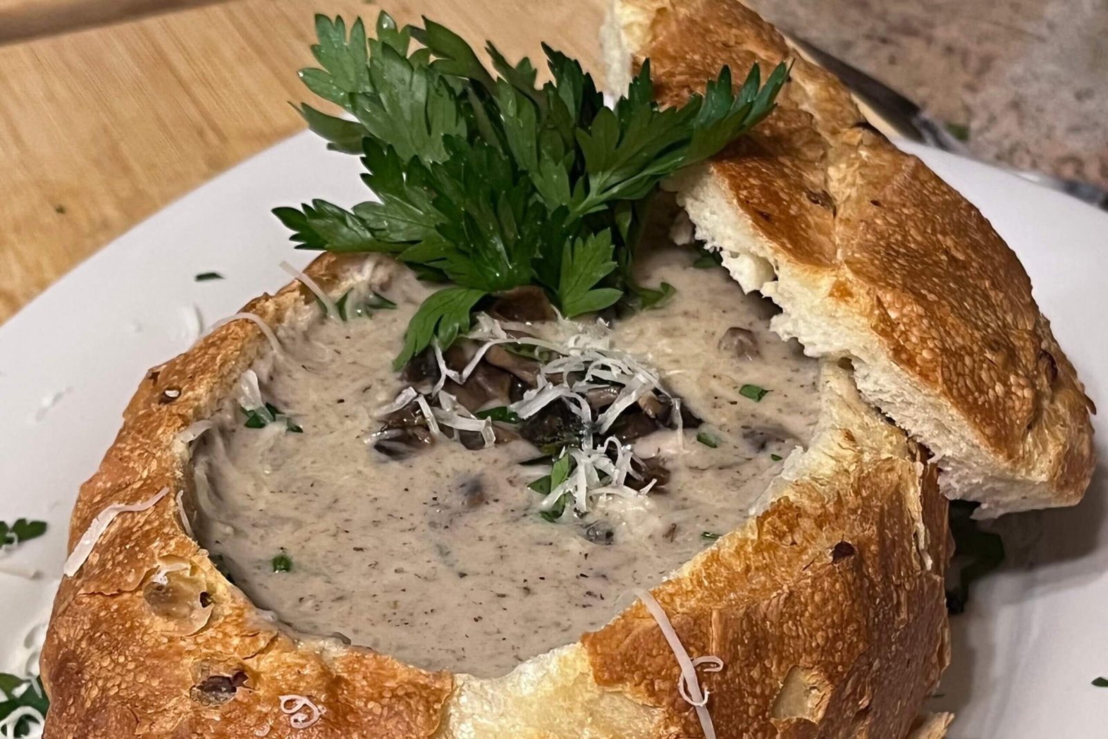 a creamy mushroom soup served in a sourdough bowl decorated with parsley and parmesan